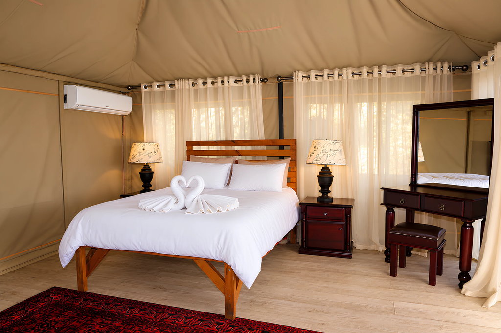 A double bed with a timber headboard between two bedside lamps, beside a dressing table and mirror.