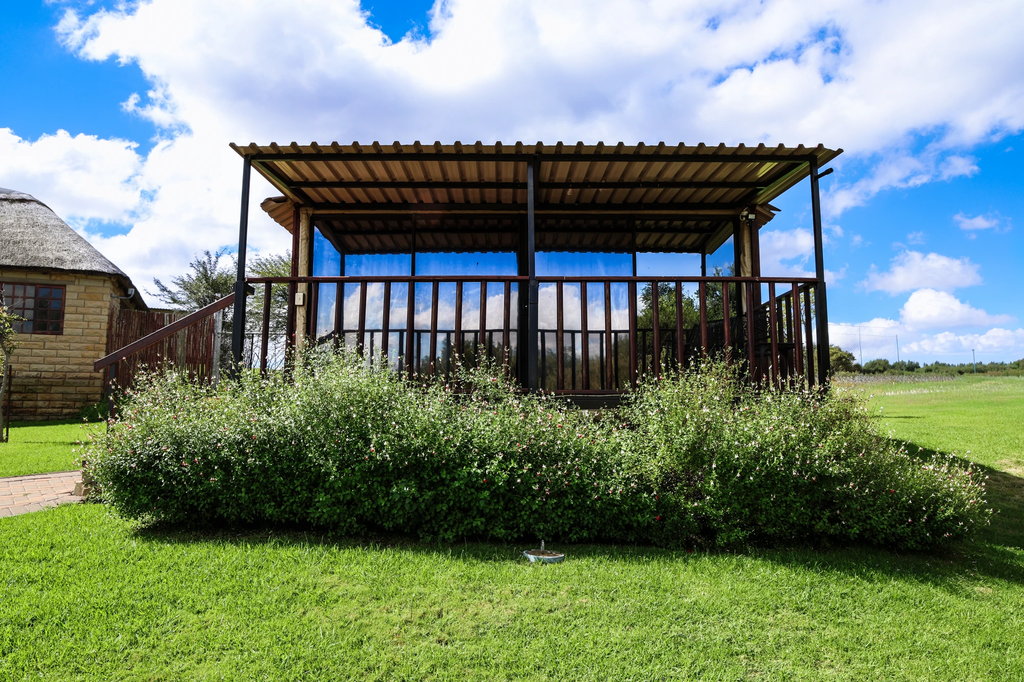 The covered timber veranda of a wooden house at Goldfields, with flowering shrubs and lawn in front.